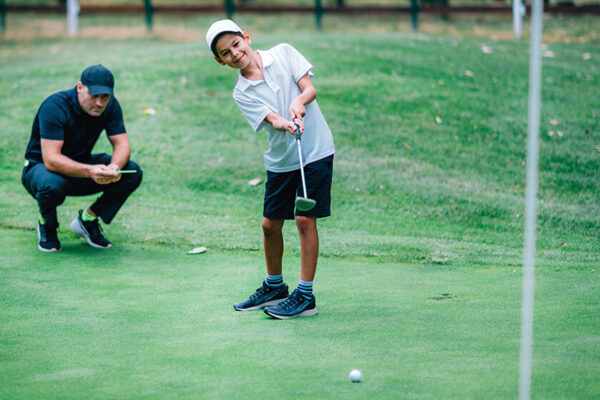 Young boy playing golf with coach watching